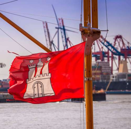 Wehende Hamburgfahne mit Hafen im Hintergund Wehende Hamburgfahne mit Hafen im Hintergund