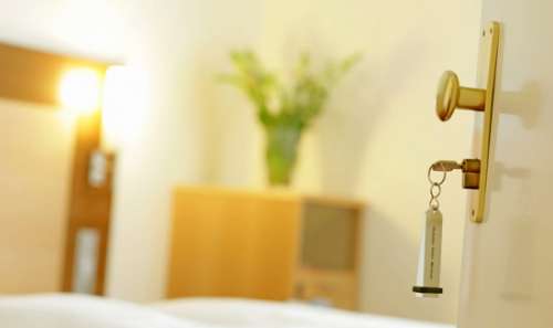 Imagefoto einer geöffneten Hotelzimmertür mit steckendem Schlüssel und Zimmer im Hintergrund.